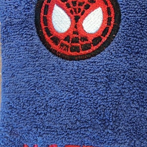 May include: Blue terry towel with a red and black Spider-Man emblem and the name "MATTIA" embroidered in red. The towel has a soft, textured surface.