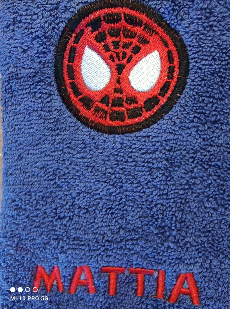 May include: Blue terry towel with a red and black Spider-Man emblem and the name "MATTIA" embroidered in red. The towel has a soft, textured surface.