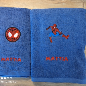 May include: Two blue bath towels with red embroidered text and Spiderman designs. One towel features the Spiderman logo, the other has a full Spiderman figure. The name "MATTIA" is embroidered in red on both towels.
