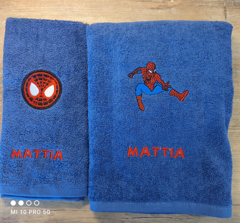 May include: Two blue bath towels with red embroidered text and Spiderman designs. One towel features the Spiderman logo, the other has a full Spiderman figure. The name "MATTIA" is embroidered in red on both towels.