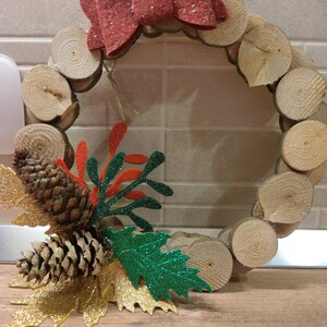 May include: A festive Christmas wreath made from wooden slices, featuring a red glitter bow, pine cones, and gold and green glitter leaves. Ideal for seasonal decoration.