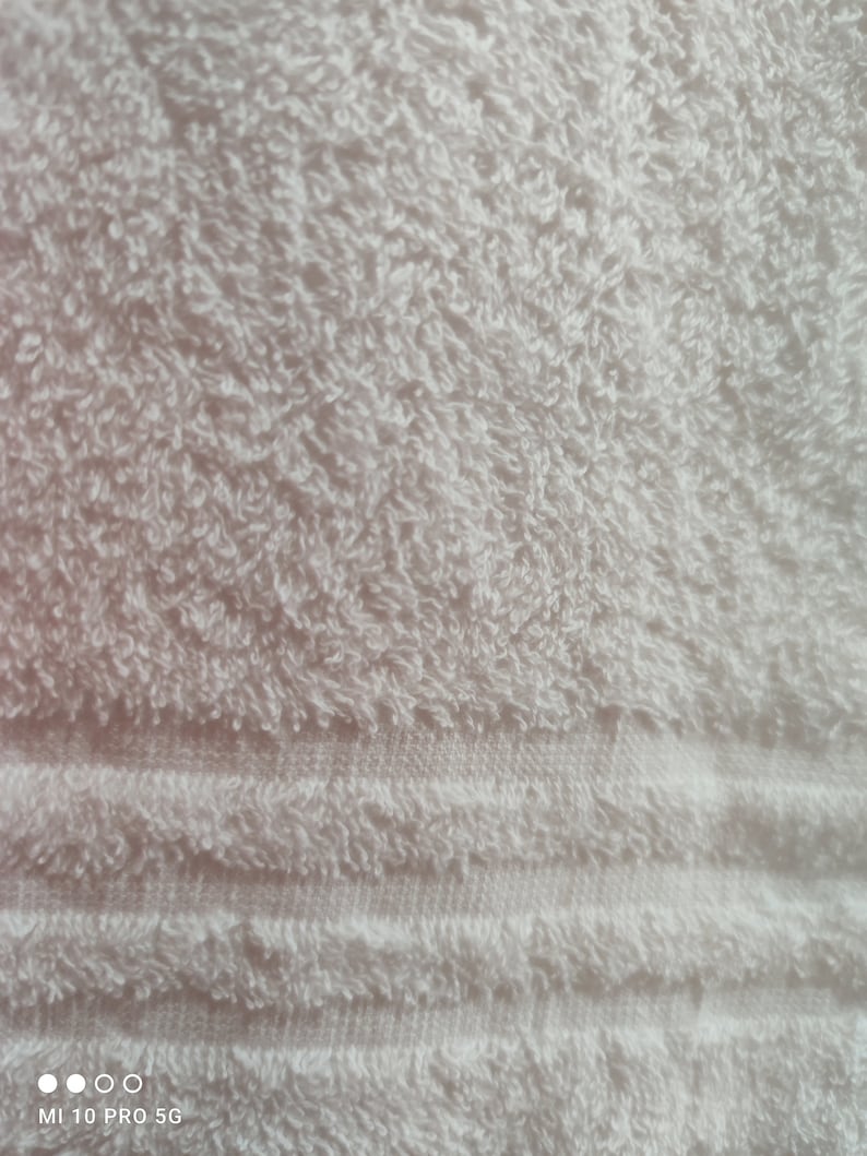 May include: Close-up of a white, fluffy towel. The terry cloth texture is visible, with a pattern of horizontal stripes near the bottom. The towel appears soft and absorbent, ideal for bathroom use.