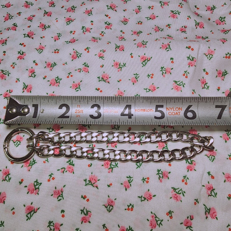 Puede incluir: Un collar de cadena de plata con cierre de anillo, medido con una regla que indica "1, 2, 3, 4, 5, 6, 7" pulgadas.