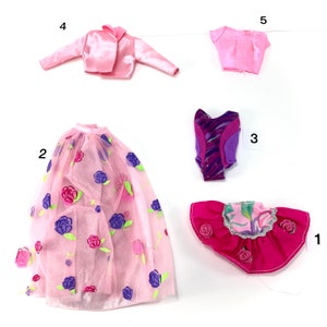 May include: Five doll clothes items, including a pink jacket, a pink skirt, a pink top, a purple and pink leotard, and a pink and purple ruffled skirt.
