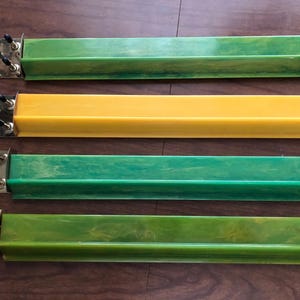 May include: Four vintage Mahjong tile racks in shades of green and yellow. Each rack has a rectangular trough design with a metal end piece featuring black knobs. The racks are arranged horizontally on a wooden surface.