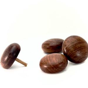 May include: Four wooden tops in varying shapes and sizes are displayed against a white background. One top is elongated with a wooden peg, while the others are rounded and smooth. The tops are a rich, dark brown color.