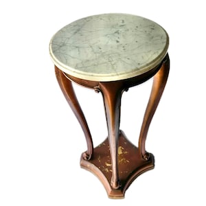 May include: A small, antique side table with a round marble top. The table has a dark brown, curved wooden base with three legs. The marble top is light gray with darker gray veining. The table is approximately 24 inches tall.
