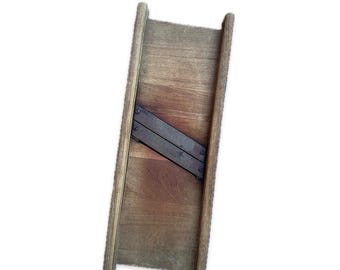 May include: A vintage wooden mandoline with a rectangular frame and a metal blade. The wood has a warm, aged tone, and the metal blade is secured with rivets. This kitchen tool is designed for slicing vegetables.