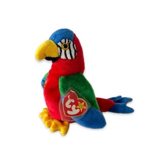 May include: A colorful plush parrot toy with a red body, green wings, and blue head and tail. The parrot has a yellow beak and feet, and a tag is attached. The toy is designed to resemble a macaw.