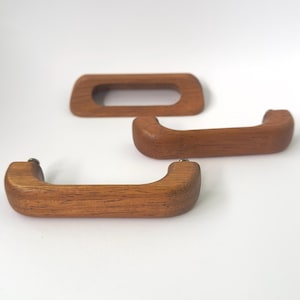 May include: Three medium-brown wooden drawer pulls with a smooth, curved design. Each handle features a visible wood grain pattern and rounded edges. The hardware is arranged with one pull positioned horizontally at the top and two below.