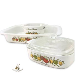 May include: A set of white ceramic baking dishes with a colorful vegetable design. The set includes a large rectangular dish, two smaller square dishes, and a square dish with a glass lid. The dishes are decorated with tomatoes, lemons, and mushrooms.