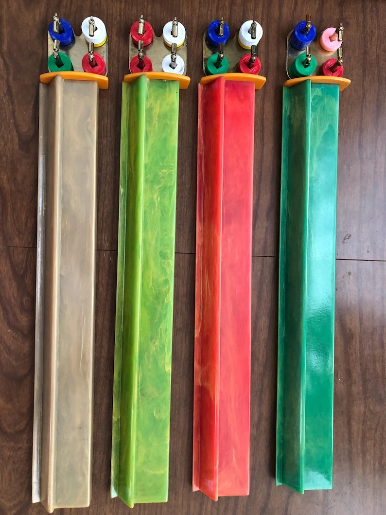 Puede incluir: Cuatro piezas de juego vintage en tonos beige, verde, rojo y verde. Cada pieza tiene una columna rectangular con una parte superior decorativa con clavijas de colores. Las partes superiores tienen herrajes de lat&oacute;n y est&aacute;n montadas sobre una base naranja.