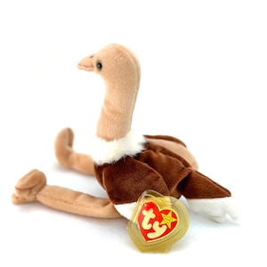 May include: A brown and tan plush toy ostrich with a white fur collar. The toy has a red and yellow Ty Beanie Baby tag attached to it.