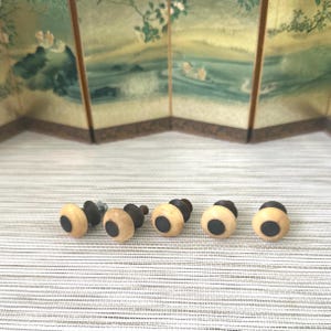May include: Five small, round cabinet knobs arranged in a horizontal row. Each knob features a smooth, cream-colored circular face with a dark brown, circular center inlay. The base of each knob is a dark brown, cylindrical mounting piece.