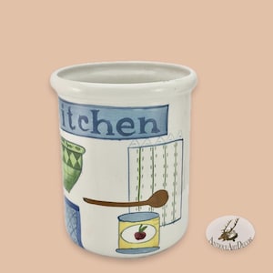 May include: White ceramic kitchen utensil holder with blue accents. The word "kitchen" is displayed on a blue banner. The holder features painted images of kitchen items, including a spoon and a can of cherries.