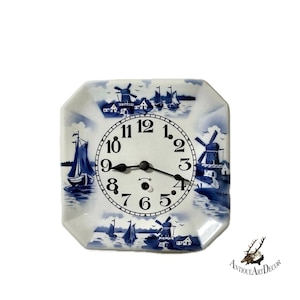 May include: A square ceramic clock with a blue and white Dutch windmill and sailboat design. The clock face has black numbers and hands. The clock is a decorative item.