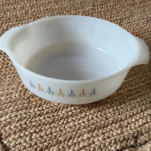 Könnte beinhalten: Ovale, weißes Auflaufform mit Griffen. Die Schüssel hat eine strukturierte Oberfläche und ist mit einem Muster aus blauen und goldenen blattartigen Designs um den Rand verziert. Ein Vintage-Küchenartikel.