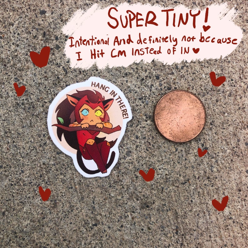 K&ouml;nnte beinhalten: Ein kleiner, runder Aufkleber mit einer Comic-Katze mit rot-orangem Fell, gelben Augen und einem wei&szlig;en Stirnband. Die Katze h&auml;lt sich an einem Ast fest und der Aufkleber sagt "Hang in there!" in einer wei&szlig;en Sprechblase.