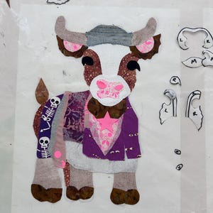 Könnte beinhalten: Ein skurriles Kuh-Applikation mit einem Patchwork-Design. Die Kuh hat ein weißes Gesicht, braune und rosa Hörner und ein lila und gemustertes Outfit. Ein rosa Stern und Skelett-Details verleihen eine einzigartige Note. Das Bild enthält Schnittmusterteile.