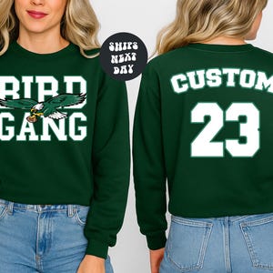 A woman wearing a green sweatshirt with the text "BIRD GANG" and the number "23" printed on it.