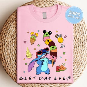 A pink t-shirt with a cartoon character, likely Stitch, enjoying various ice cream flavors and a drink. The text on the t-shirt says "Best Day Ever".