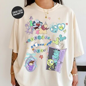a person wearing a white t-shirt with a colorful graphic design depicting various cartoon characters and scenes from the movie Monsters, Inc.