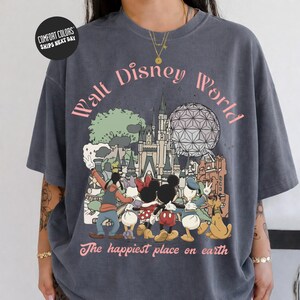 A person wearing a gray t-shirt with a graphic design featuring Disney characters and landmarks, including Mickey Mouse, Minnie Mouse, Donald Duck, and the Eiffel Tower.