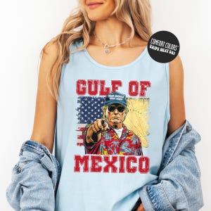 A woman wearing a tank top with a graphic design of a man pointing at the word "GULF" and "MEXICO" printed on it.