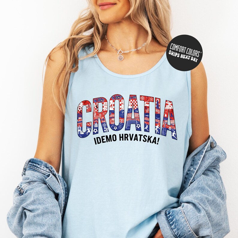 A woman wearing a light blue tank top with the word "Croatia" printed on it, along with the phrase "IDEMO HVRVATSKA!" printed below. She is also wearing a denim jacket and has a necklace around her neck.