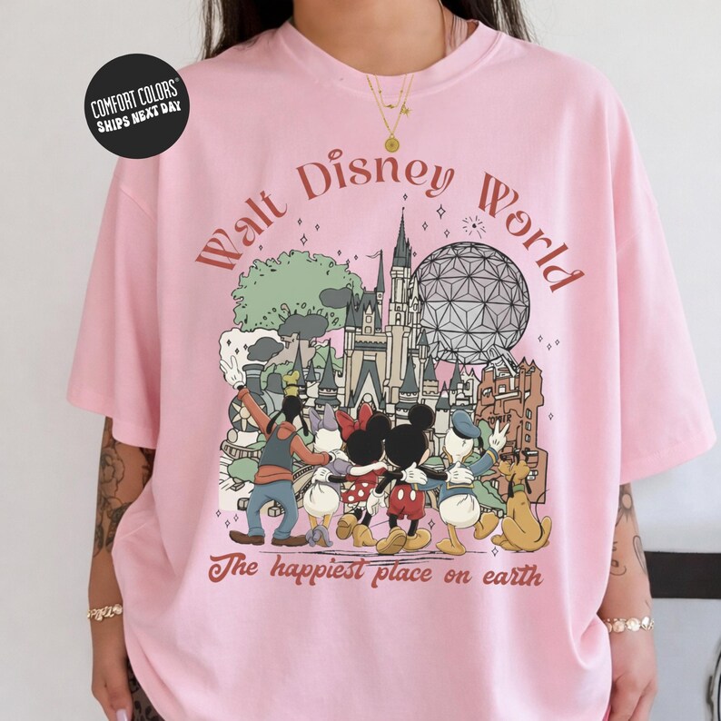 A pink t-shirt with a graphic design featuring Disney characters and landmarks, including the Eiffel Tower and the castle.