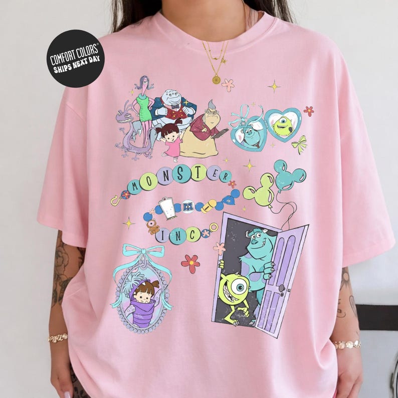 The image is a pink t-shirt with various cartoon characters and designs, including a character with a heart-shaped headband, a character with a blue heart, and a character with a green heart.