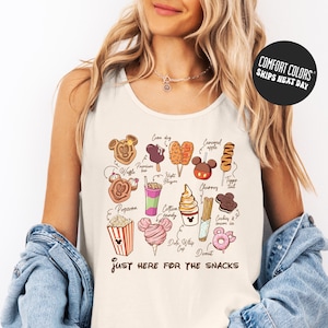 A woman wearing a white tank top with a graphic design of various Disney-themed snacks and treats, including popcorn, cotton candy, hot dogs, and ice cream cones.