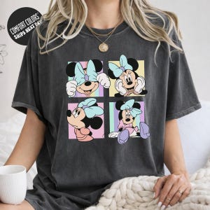 A person wearing a gray t-shirt with a graphic of Minnie Mouse in pastel colors.