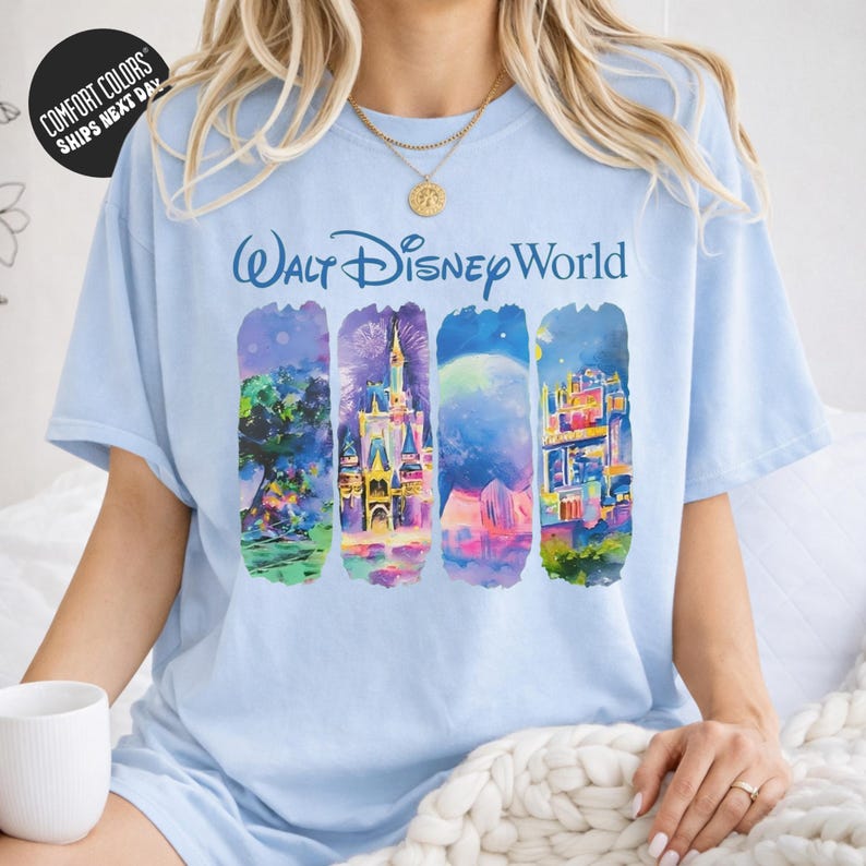 A woman wearing a light blue t-shirt with a colorful graphic design depicting various scenes from Walt Disney World.