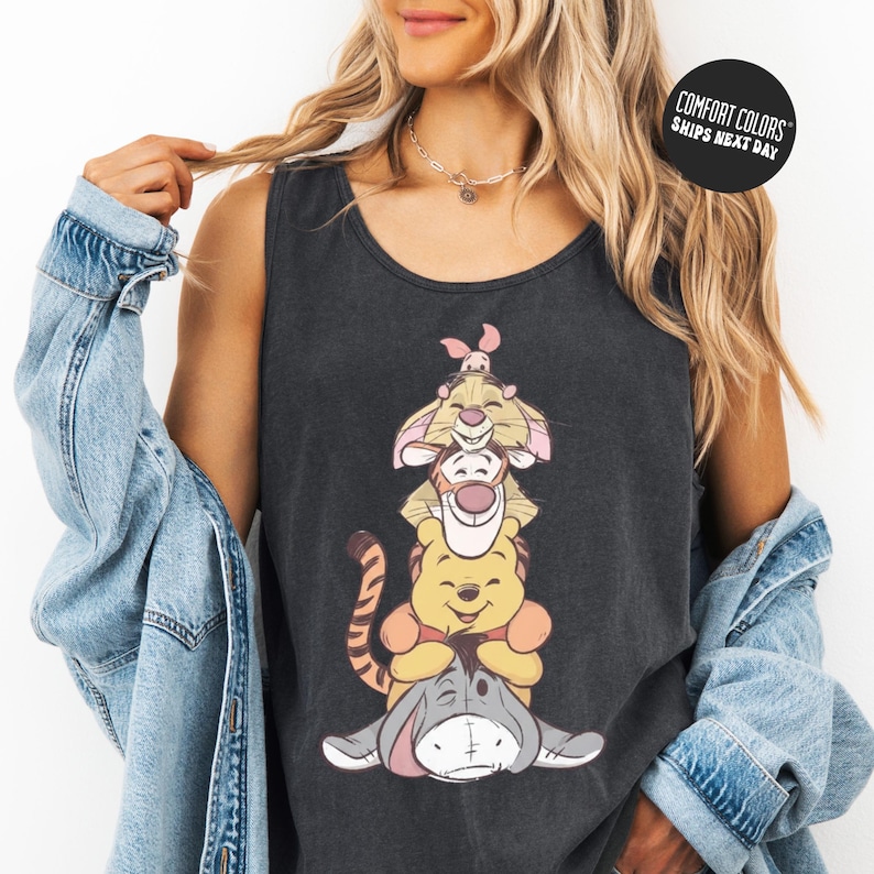 A woman wearing a black tank top with a cartoon character design and a denim jacket.