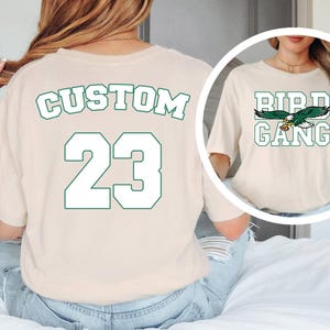 A woman wearing a white t-shirt with the text "CUSTOM 23" printed on it, along with a graphic of a bird.
