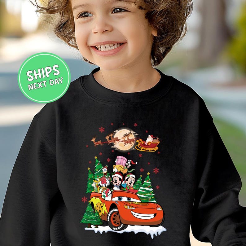 A young child wearing a black sweater with a Christmas-themed design featuring a red car, Santa Claus, and other holiday characters.