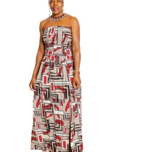May include: A woman wearing a strapless maxi dress with a geometric pattern in shades of red, black, and beige. She is wearing a beaded necklace and has her hair pulled back in a bun.