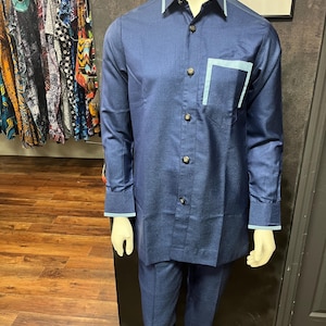 May include: A navy blue long-sleeved shirt with a light blue trim on the collar and cuffs. The shirt has a single chest pocket with a light blue trim. The shirt is paired with matching navy blue pants.
