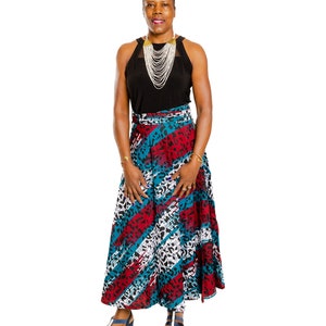May include: A woman wearing a black sleeveless top with a layered silver and gold necklace, a long wrap skirt with a blue, red, and white geometric pattern, and blue sandals.