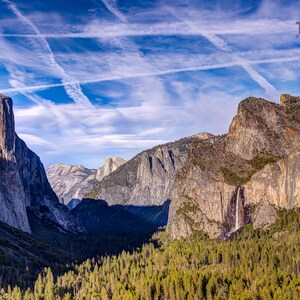 May include: A scenic landscape photograph of Yosemite Valley, featuring towering granite cliffs, a waterfall, and a lush forest. The sky is a vibrant blue with contrails. The image is labeled "Thin Air Photography."