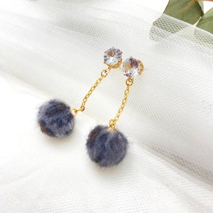May include: A pair of dangle earrings with a clear rhinestone at the top and a gray fluffy pom-pom at the bottom.