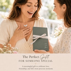 May include: A woman smiles while receiving a gift. The gift is a dark green book tied with a light ribbon. The book has the words "HOPE LOVE Shine" printed on it. The woman is wearing a silver necklace.