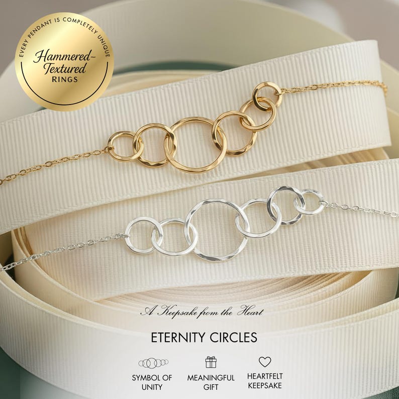 May include: Two necklaces with interlocking circles, one gold and one silver, rest on a white ribbon. The gold necklace has a chain and six circles. The silver necklace has a chain and five circles. The image includes text that reads "Eternity Circles."