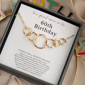 May include: Gold-toned necklace with six interlocking rings, presented in a gift box. The card inside reads "60th Birthday" and includes a message about celebrating six decades. The necklace is a thoughtful gift.