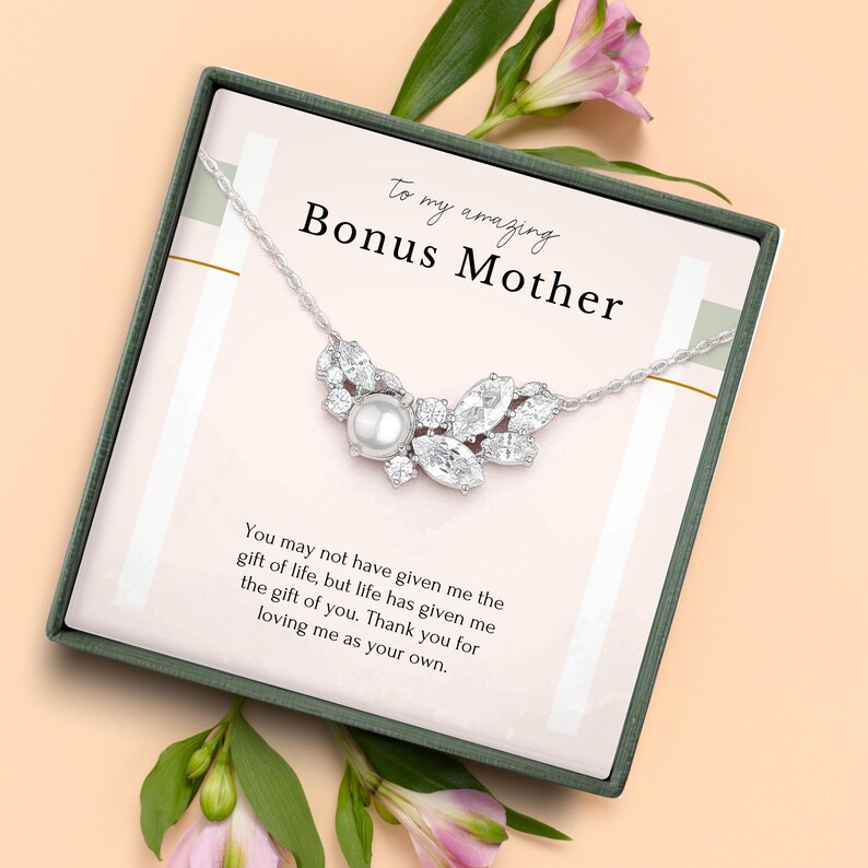 May include: A silver necklace with a pearl and crystal pendant, presented in a gift box with the text "To my amazing Bonus Mother". The box is decorated with pink flowers and a message of appreciation.