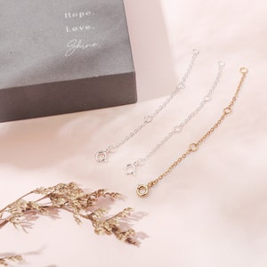 May include: Three silver and gold chain extenders for jewelry making. The extenders are on a white surface.