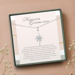 K&ouml;nnte beinhalten: Eine silberne Halskette mit einem Nordstern-Anh&auml;nger, pr&auml;sentiert in einer Geschenkbox. Der Anh&auml;nger hat ein Sternenmuster mit einem zentralen Edelstein. Der Text "North Star Guiding Light" ist auf der Karte aufgedruckt.