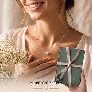 May include: A woman wearing a delicate silver necklace with a single pearl pendant. She is holding a bouquet of white flowers and a teal gift box tied with a ribbon. The text "Perfect Gift For Her" is displayed below.