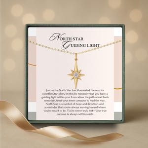 K&ouml;nnte beinhalten: Eine goldfarbene Halskette mit einem Nordstern-Anh&auml;nger, pr&auml;sentiert in einer Geschenkbox. Der Anh&auml;nger hat ein Sternenmuster mit einem zentralen Edelstein. Die Box tr&auml;gt den Text "North Star Guiding Light" und eine Botschaft &uuml;ber Hoffnung.